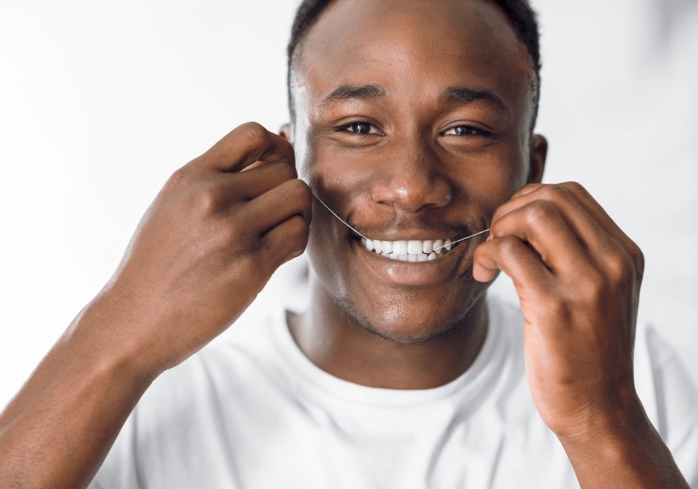 Happy Black Man Flossing Teeth Using Dental Floss In Bathroom