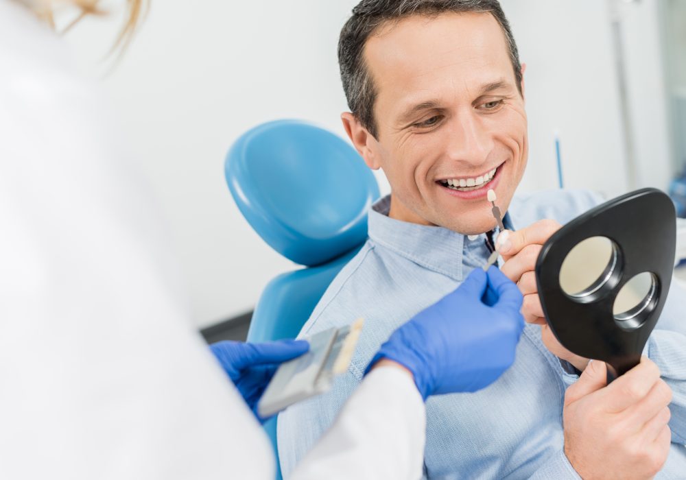 Male patient choosing tooth implant looking at mirror in modern dental clinic